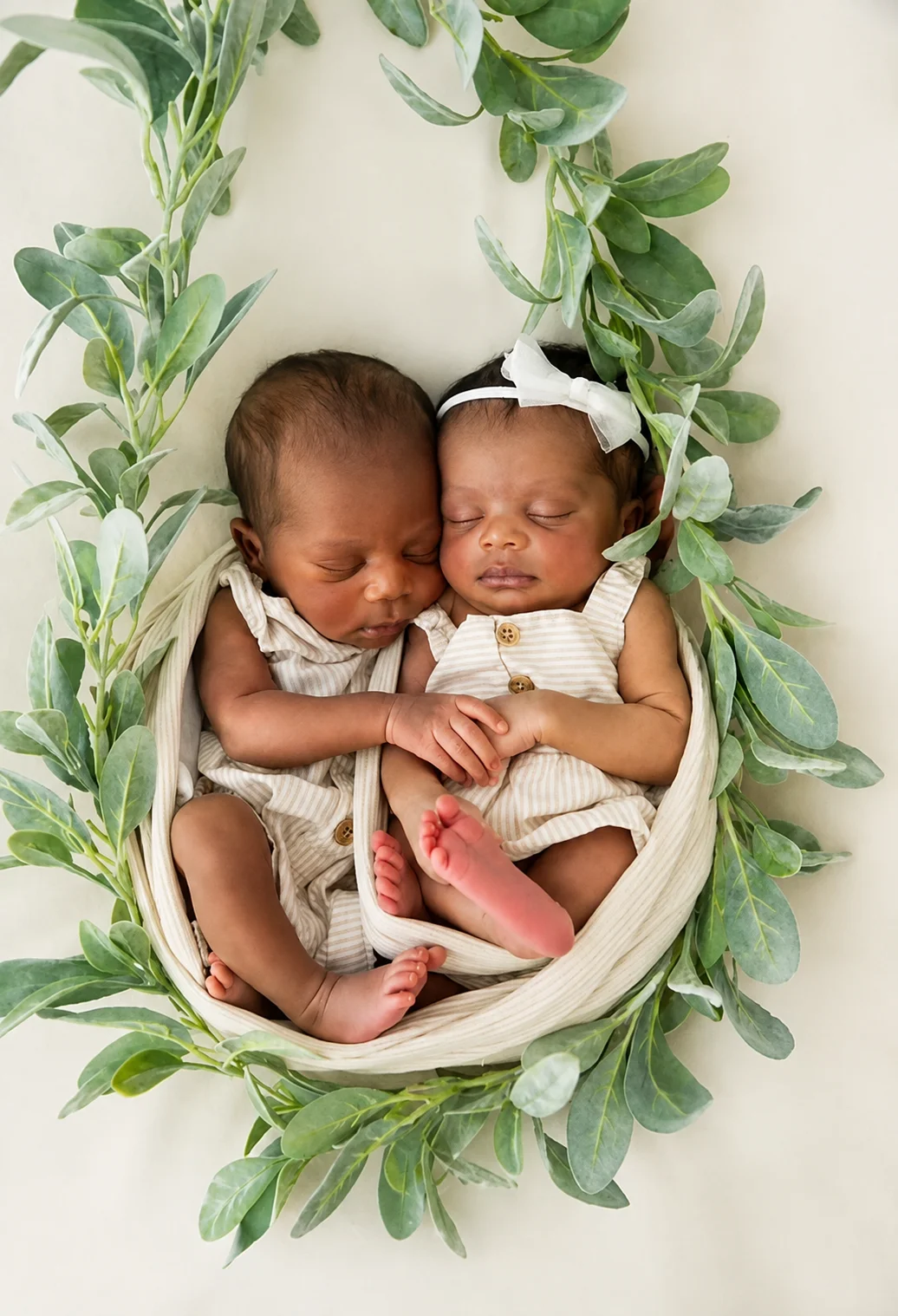 Newborn twins resting together in a cream hammock surrounded by green leaves